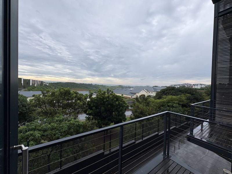 A modern balcony featuring timber decking and a sleek metal balustrade, offering an elevated view of the surrounding landscape and residential area.