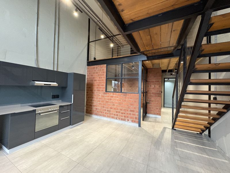 Modern industrial-style open plan apartment featuring a sleek kitchen, exposed brickwork, and a striking timber and steel staircase leading to a mezzanine level.
