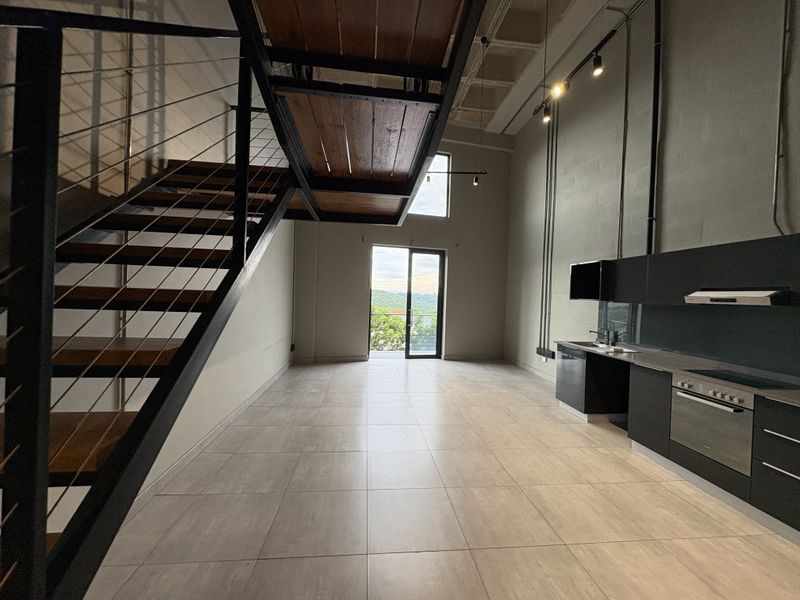 Spacious open-plan living area featuring an industrial-style staircase, modern kitchen with built-in appliances, and large sliding doors leading to an outdoor space.