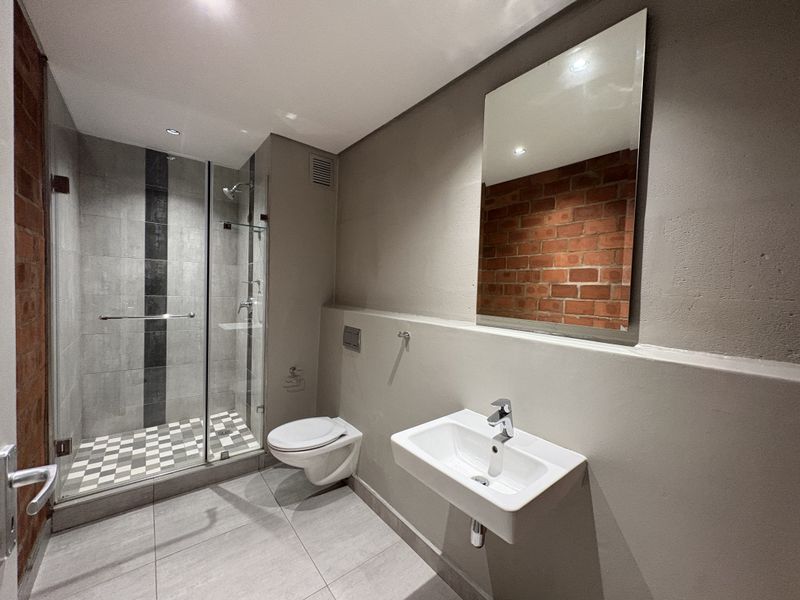 Modern bathroom featuring a glass-enclosed shower, wall-mounted basin, and a stylish exposed brick feature wall with contemporary finishes.