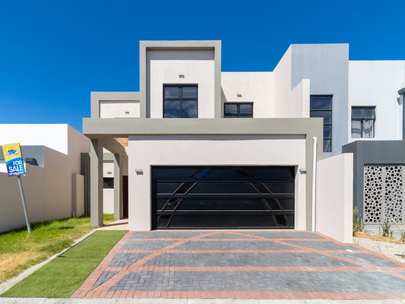 Modern double-story residential facade featuring a sleek black garage door, paved driveway, and contemporary architectural design with decorative metal screening.