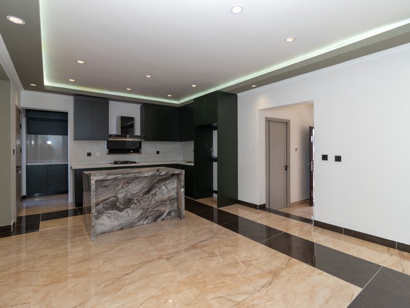 Modern kitchen featuring dark cabinetry, a striking stone-topped island, and polished tiled flooring with integrated recessed and cove lighting.