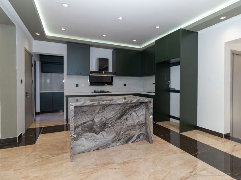 Modern kitchen featuring a striking marble island, dark cabinetry, integrated gas hob, extractor fan, and elegant recessed ceiling lighting with tiled flooring.