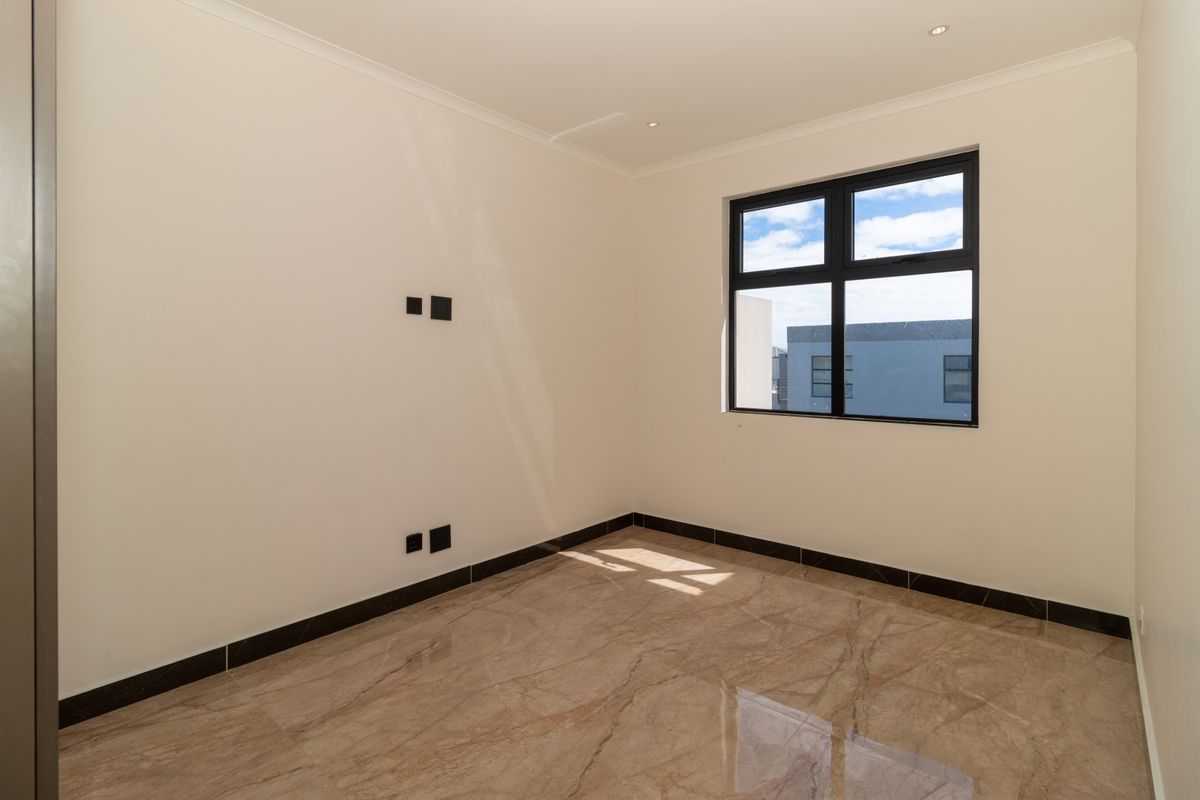 A bright, empty bedroom featuring polished marble-look floor tiles, neutral walls, and a modern black-framed window.