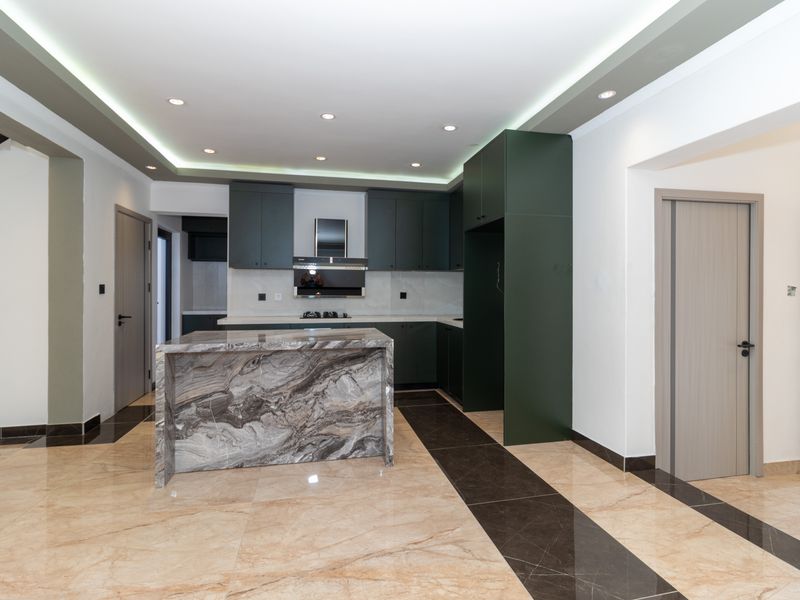 Modern kitchen featuring dark green cabinetry, a striking marble-topped island, integrated appliances, and high-quality tiled flooring with recessed ceiling lighting.