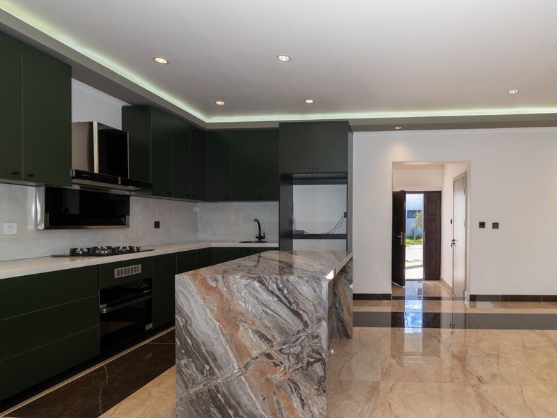 Modern kitchen featuring dark green cabinetry, a striking stone-topped island, integrated appliances, and polished marble-style flooring with recessed and cove lighting.