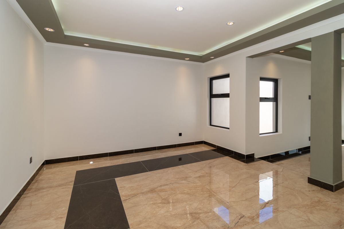 A bright, modern, and empty living area featuring polished porcelain floor tiles, recessed ceiling lighting, and contemporary architectural detailing.