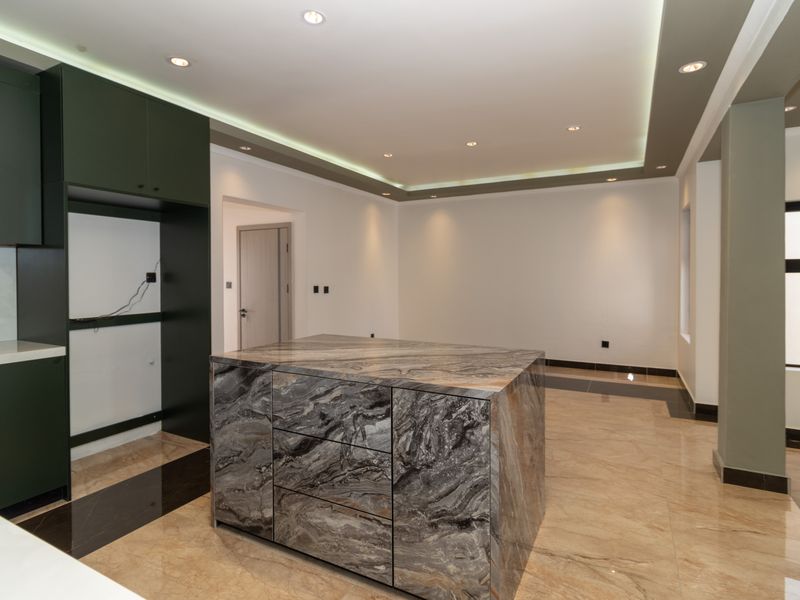 Modern kitchen featuring a striking marble island, sleek dark cabinetry, and sophisticated recessed cove lighting in an open-plan layout.