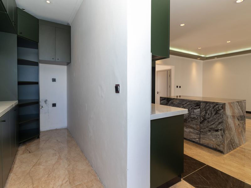 Modern kitchen area featuring dark green cabinetry, stone countertops, and a central island with stone finish, currently in a near-complete state.