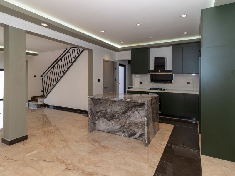 Modern open-plan kitchen featuring a striking marble island, dark cabinetry, integrated appliances, and sleek tiled flooring, seamlessly connected to the staircase area.