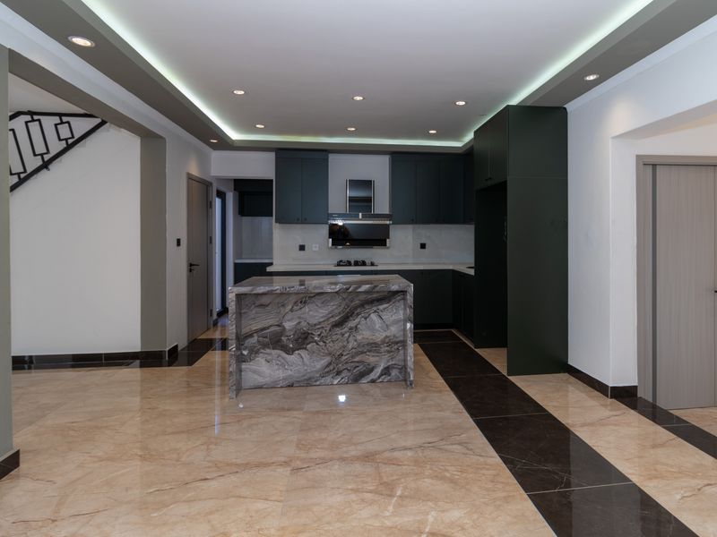 Modern open-plan kitchen featuring a striking marble island, dark cabinetry, and high-end finishes, seamlessly integrated into the living space.