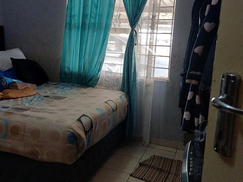 A compact bedroom featuring tiled flooring and a window fitted with security bars, offering a functional space with potential for cosmetic updates.
