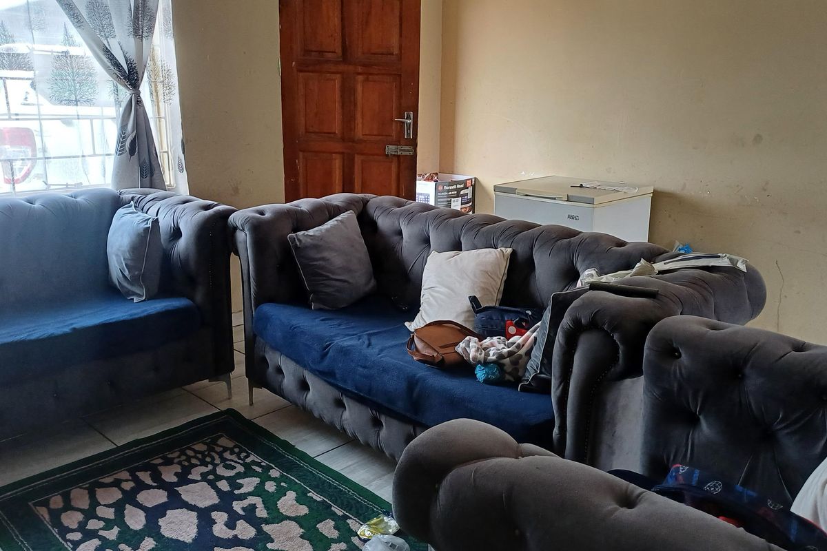 A living room area featuring tiled flooring and a wooden door, currently showing signs of wear on the wall surfaces.