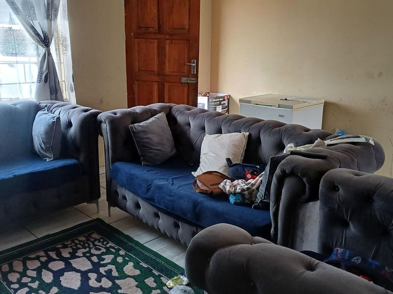 A living room area featuring tiled flooring and a wooden door, currently showing signs of wear on the wall surfaces.