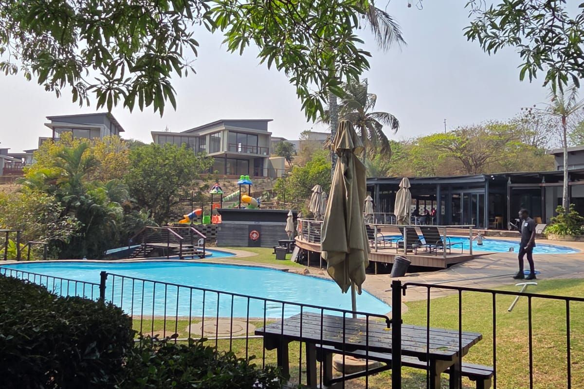 Outdoor communal pool area featuring a swimming pool, wooden decking, and landscaped surroundings within a residential estate.