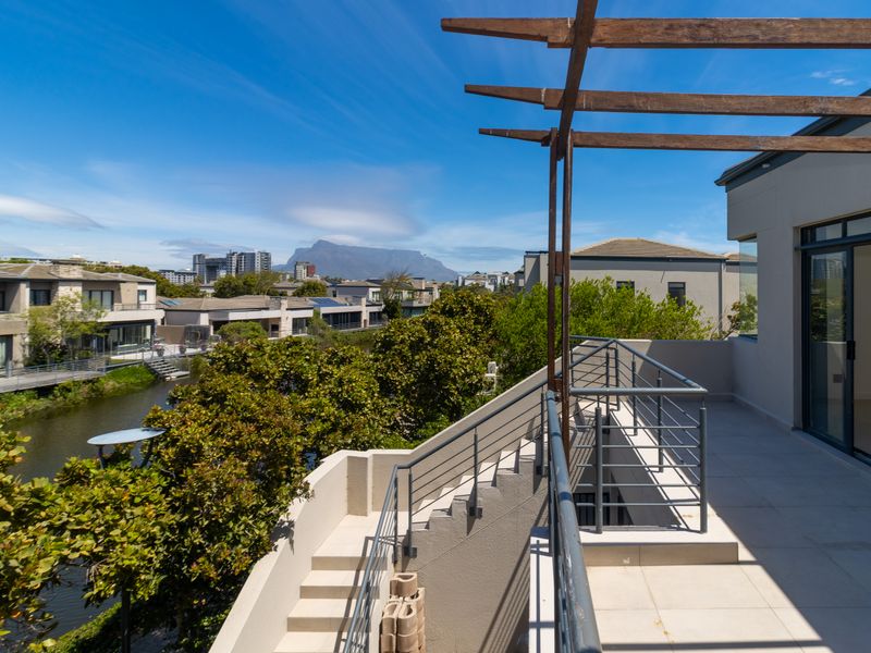 Spacious balcony featuring a timber pergola, metal balustrades, and tiled flooring, offering scenic views of the surrounding estate and mountain.
