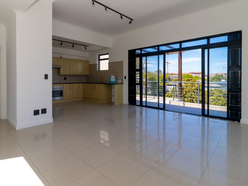 Spacious open-plan living area featuring tiled floors, a functional kitchen with built-in cabinetry, and large sliding doors leading to a private balcony.