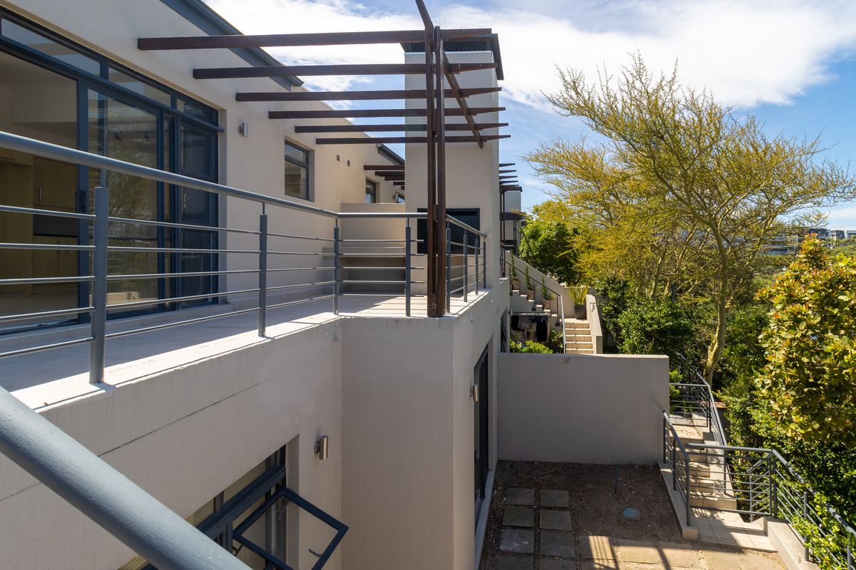Rear elevation of the townhouse featuring a spacious patio with a timber pergola, built-in braai, and metal balustrades overlooking the garden area.