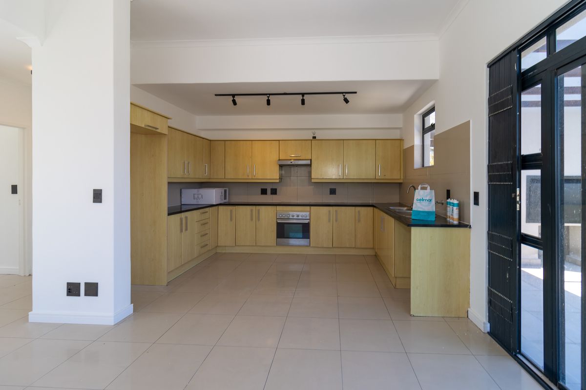 Spacious kitchen featuring light wood cabinetry, dark countertops, integrated oven, extractor fan, and tiled flooring with direct access to the exterior.