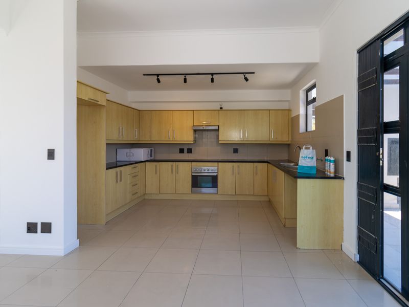 Spacious kitchen featuring light wood cabinetry, dark countertops, integrated oven, extractor fan, and tiled flooring with direct access to the exterior.