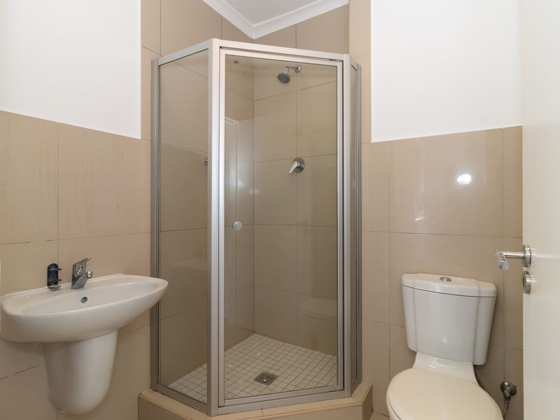 A functional bathroom featuring a corner shower enclosure, pedestal washbasin, and toilet with neutral wall tiling.