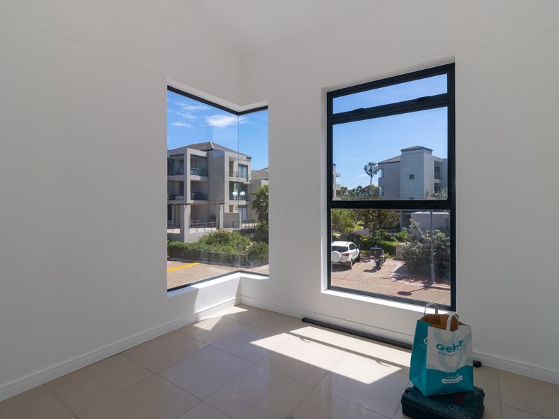 A bright, empty living area featuring modern tiled flooring and large corner windows that provide ample natural light and views of the surrounding complex.