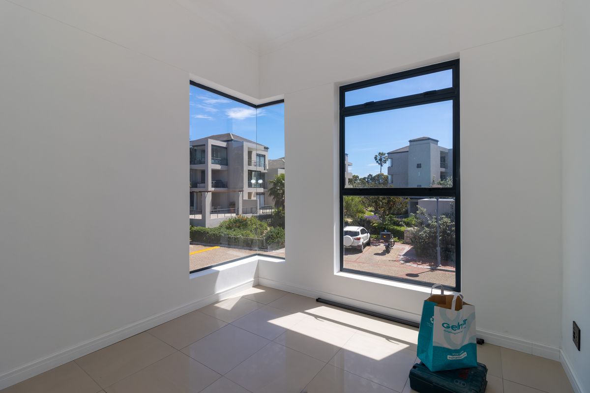 A bright, empty living area featuring modern tiled flooring and large corner windows that provide ample natural light and views of the surrounding complex.