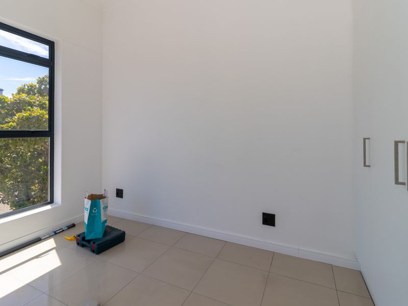 A bright, empty bedroom featuring modern tiled flooring, built-in cupboards, and a large window providing natural light.