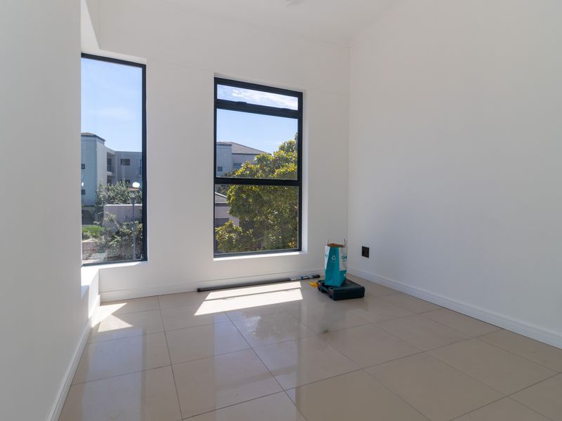 A bright, empty bedroom featuring neutral tiled flooring, modern aluminium-framed windows, and clean white walls, offering a versatile space ready for personalization.
