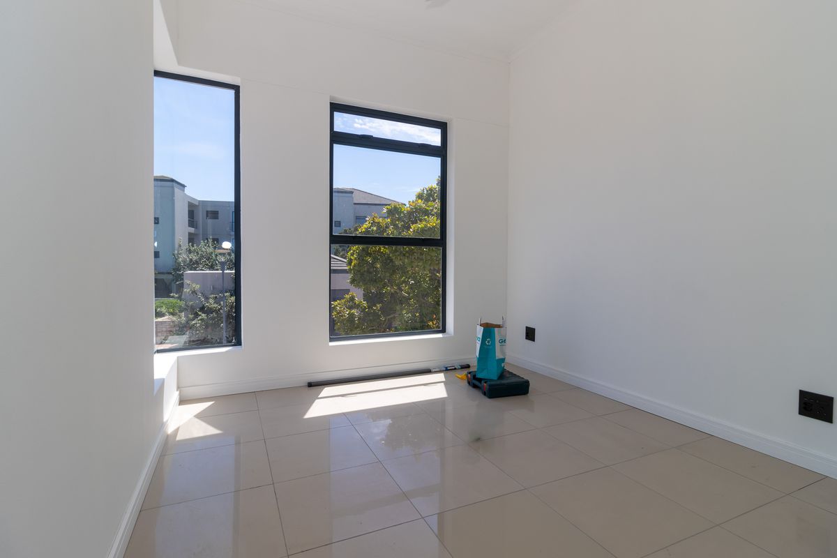 A bright, empty bedroom featuring neutral tiled flooring, modern aluminium-framed windows, and clean white walls, offering a versatile space ready for personalization.