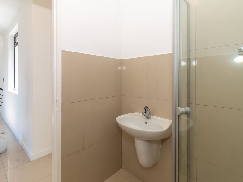 A functional bathroom featuring a pedestal basin and a glass-enclosed shower with neutral wall tiling.