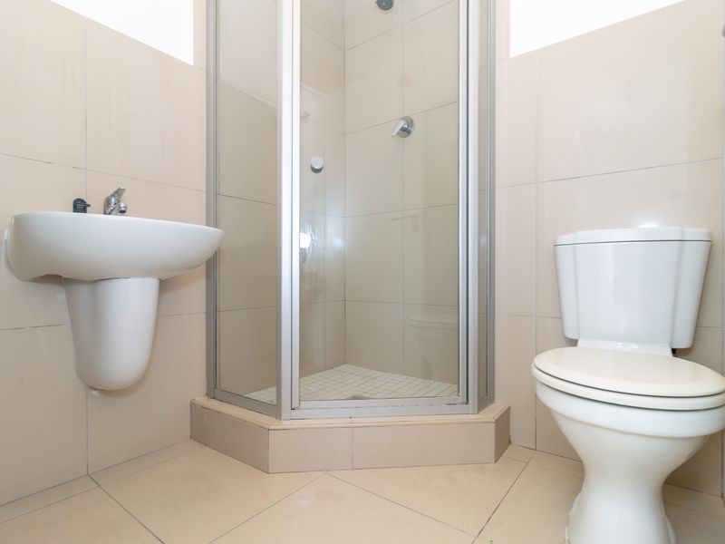 A functional bathroom featuring a corner shower enclosure, wall-mounted basin, and toilet with neutral ceramic tiling throughout.