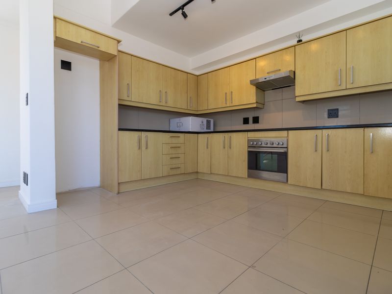 A clean, empty kitchen featuring light wood-finish cabinetry, integrated stainless steel oven and extractor fan, dark countertops, and neutral tiled flooring.