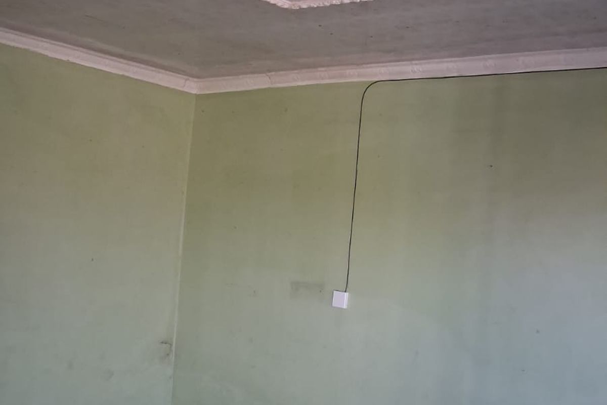 An empty living room featuring tiled flooring and a decorative ceiling rose with cornice detailing, requiring minor cosmetic updates to the walls.