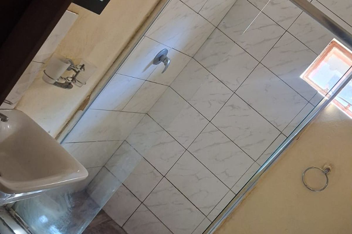 A functional bathroom featuring a glass-enclosed shower, wall-mounted basin, and toilet, currently requiring cosmetic repairs to the wall finishes and floor tiling.