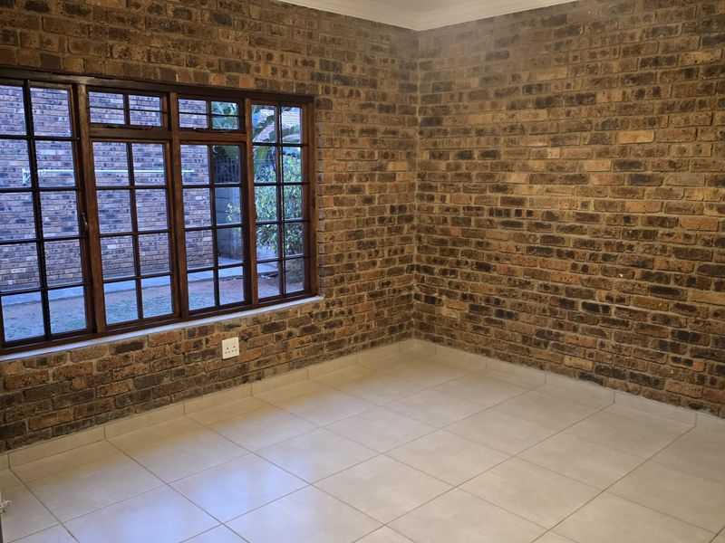 A bright, empty bedroom featuring exposed brick walls, tiled flooring, and a ceiling fan, offering a clean and versatile space.