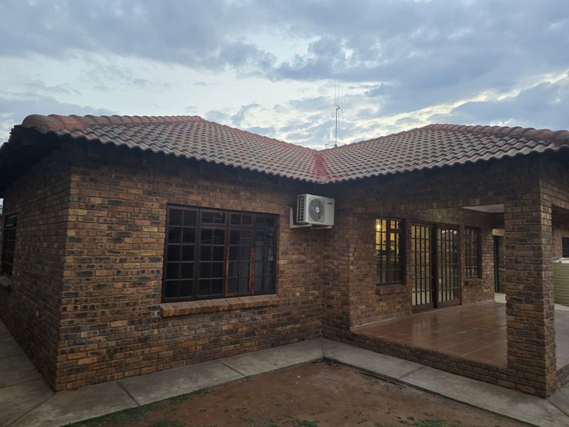 Rear view of a face brick townhouse featuring a covered patio, tiled roof, and timber window and door frames.