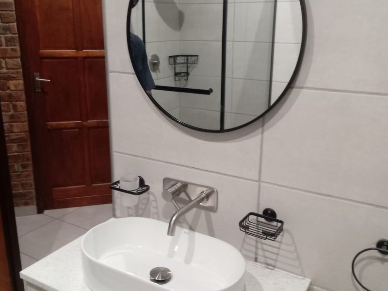 Modern bathroom featuring a vessel sink on a stone vanity, wall-mounted faucet, round mirror, and a tiled shower area with a rain shower head.