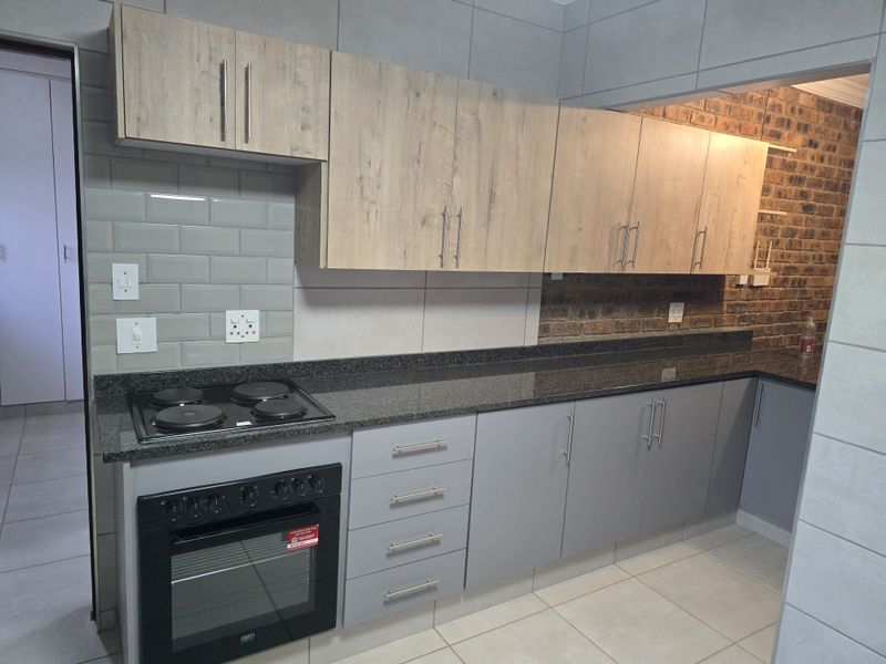 Modern kitchen featuring light wood and grey cabinetry, granite countertops, built-in oven and hob, subway tile backsplash, and an exposed brick feature wall.