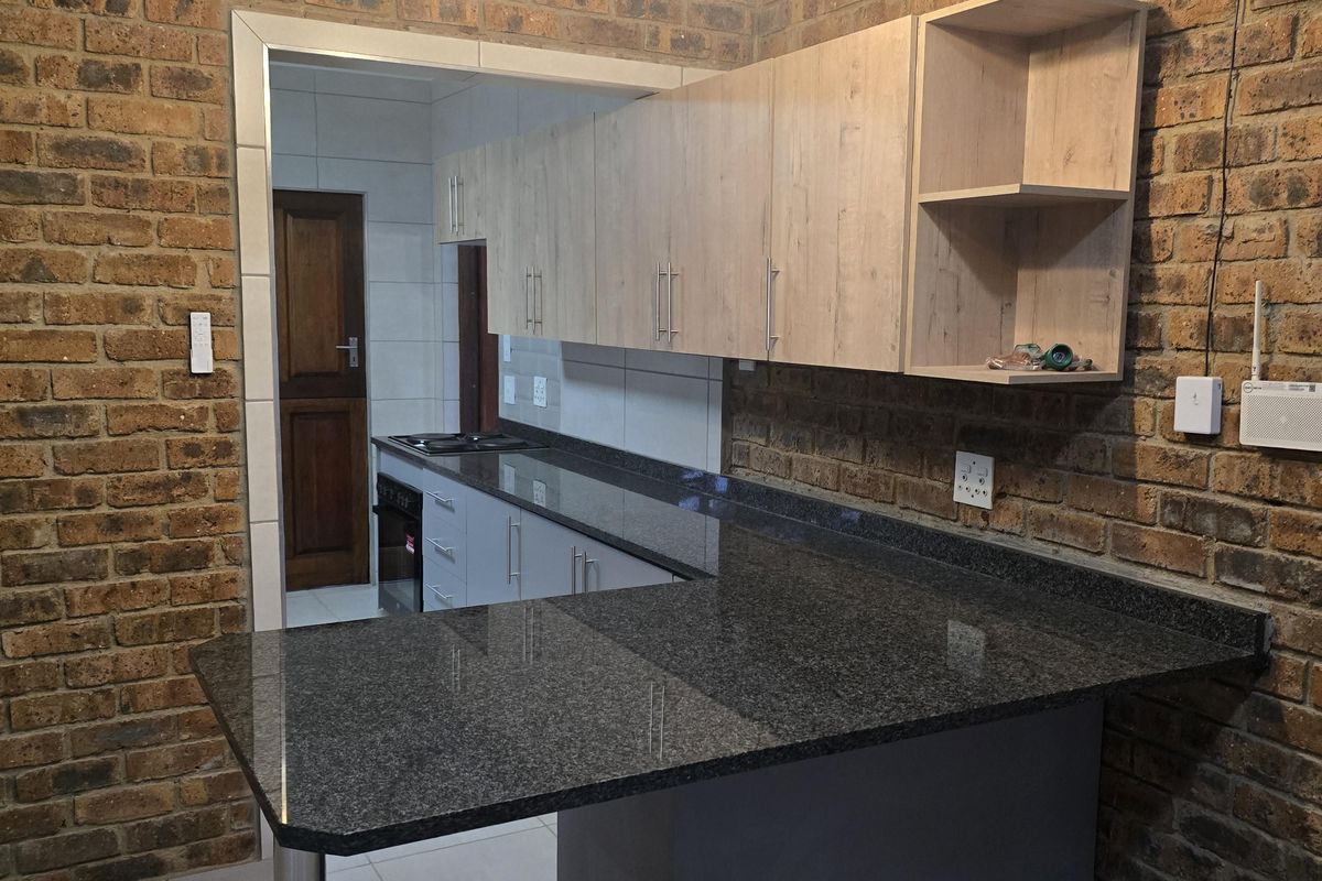 Modern kitchen featuring exposed brick walls, granite countertops, breakfast bar, and ample built-in cabinetry with a seamless transition to the scullery area.