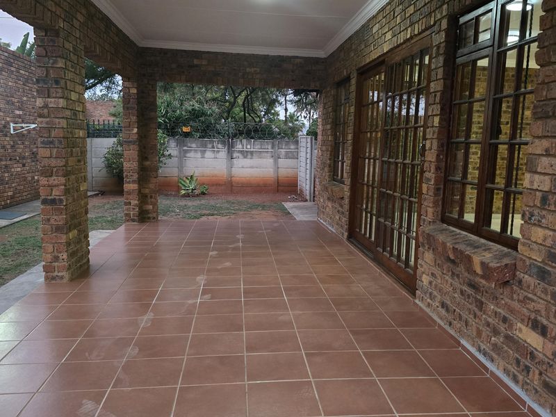 A spacious covered patio featuring exposed brickwork, tiled flooring, and direct access to the interior through sliding glass doors.