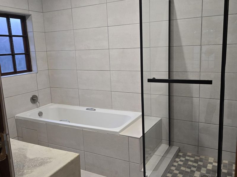 Modern bathroom featuring a built-in bathtub, a separate walk-in shower with a black-framed glass enclosure, and neutral floor-to-ceiling tiling.