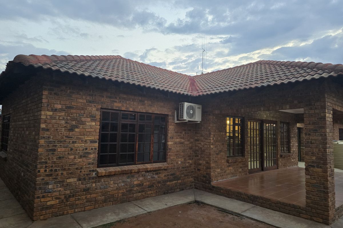 Rear view of a face brick townhouse featuring a covered patio, tiled roof, and timber window and door frames.