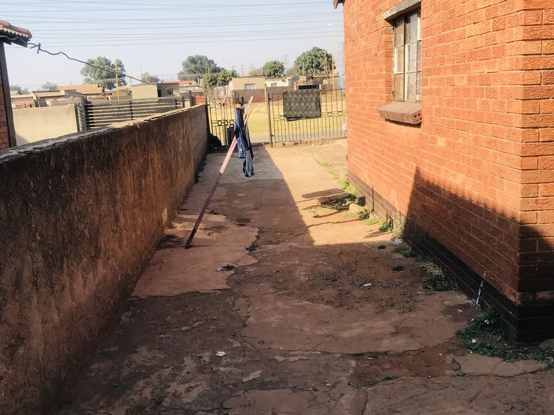 A side yard area featuring a brick exterior wall, cracked concrete paving, and a perimeter boundary wall with metal gate access.