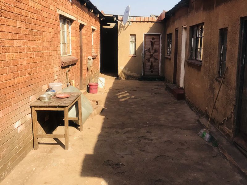A narrow exterior passage between two residential structures featuring exposed brick and plastered walls with metal window frames.