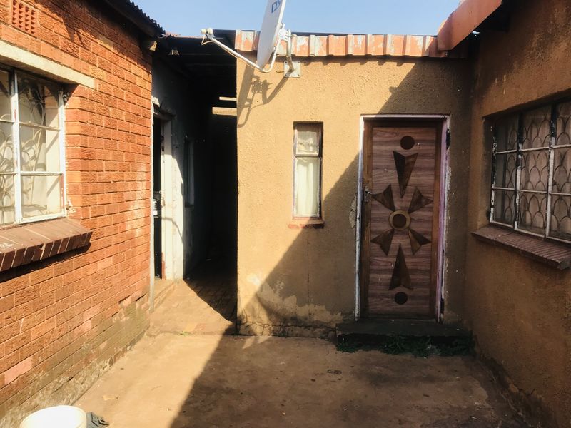 Rear exterior view of the property featuring a mix of brick and plastered walls, security bars on windows, and a paved courtyard area.