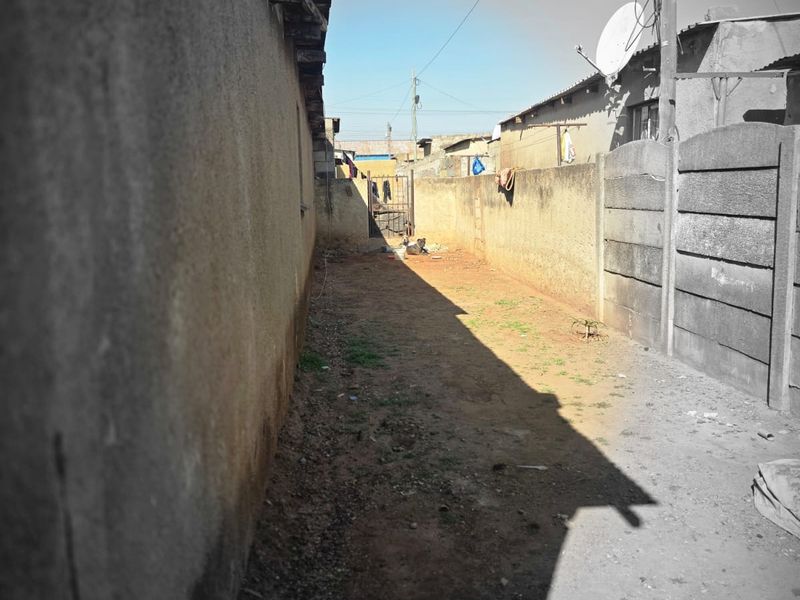 A narrow side or rear yard area featuring high boundary walls and a metal gate, requiring landscaping and surface improvements.
