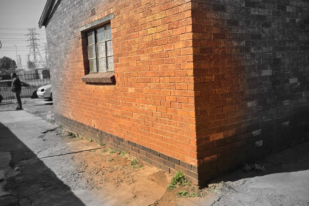 Exterior view of a brick house showing weathered masonry and cracked concrete paving surrounding the structure.
