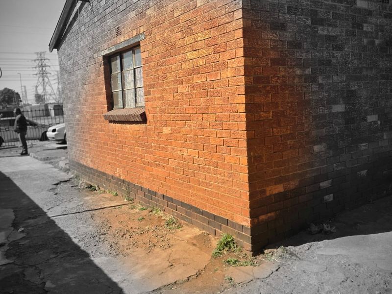 Exterior view of a brick house showing weathered masonry and cracked concrete paving surrounding the structure.
