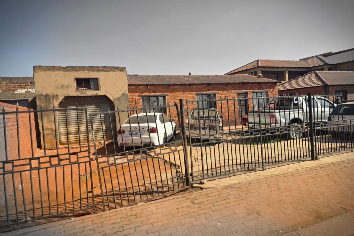 Front view of a single-story brick house featuring a metal security gate, roller shutter garage, and tiled roof.